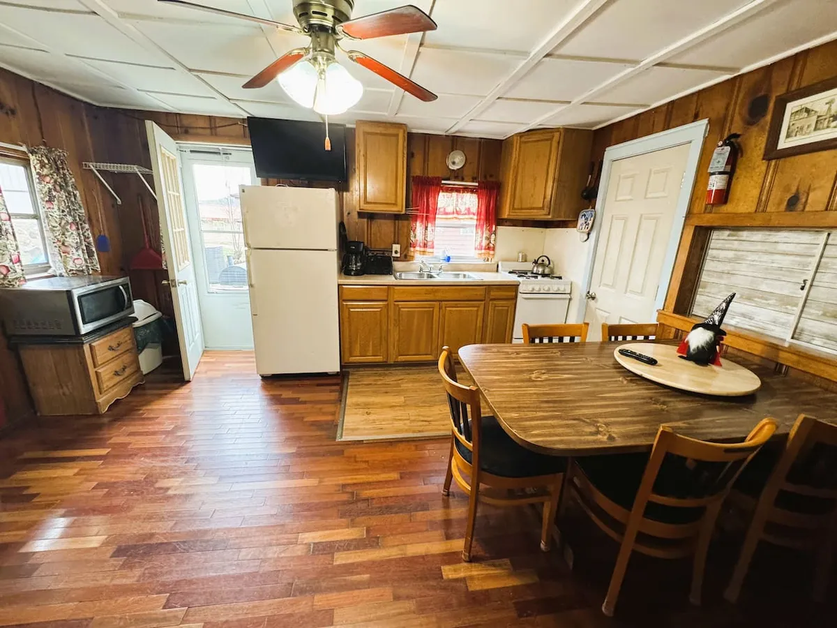 An inviting kitchen scene with a table set near a window, a refrigerator, and bright light streaming in. The space feels airy and functional, suggesting a welcoming area for meals or morning coffee while enjoying views outside.