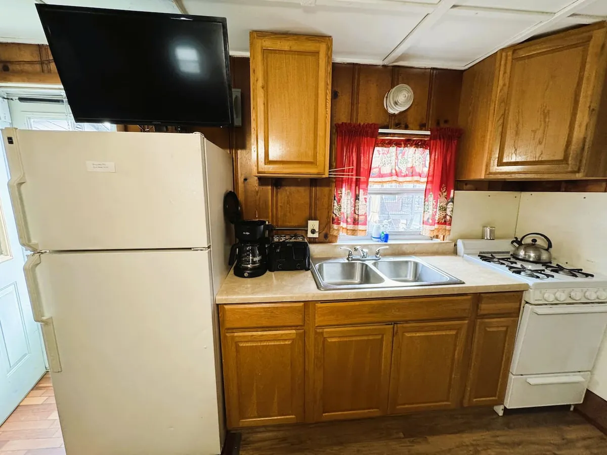 This interior image features the kitchenette area with visible sink and countertops, red curtains adding a pop of color, and various appliances suited for preparing meals. The inviting setup hints at both practicality and comfort, supporting activities like cooking, baking, and gathering with loved ones.