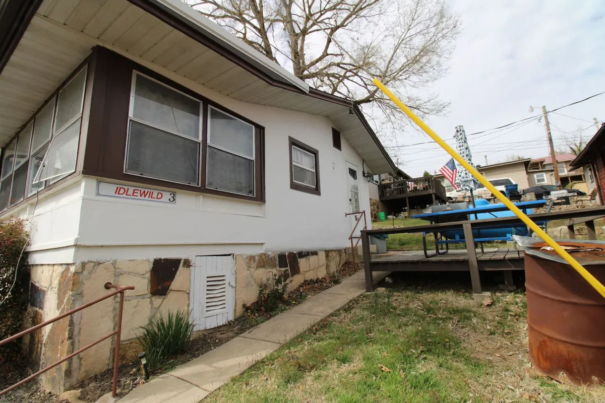 This exterior shot showcases the cabin's deck area, complete with a sunny atmosphere, yellow railing, and hints of a barbecue setup. The American flag and welcoming mood highlight the space's suitability for outdoor grilling, relaxing, or enjoying meals outside.