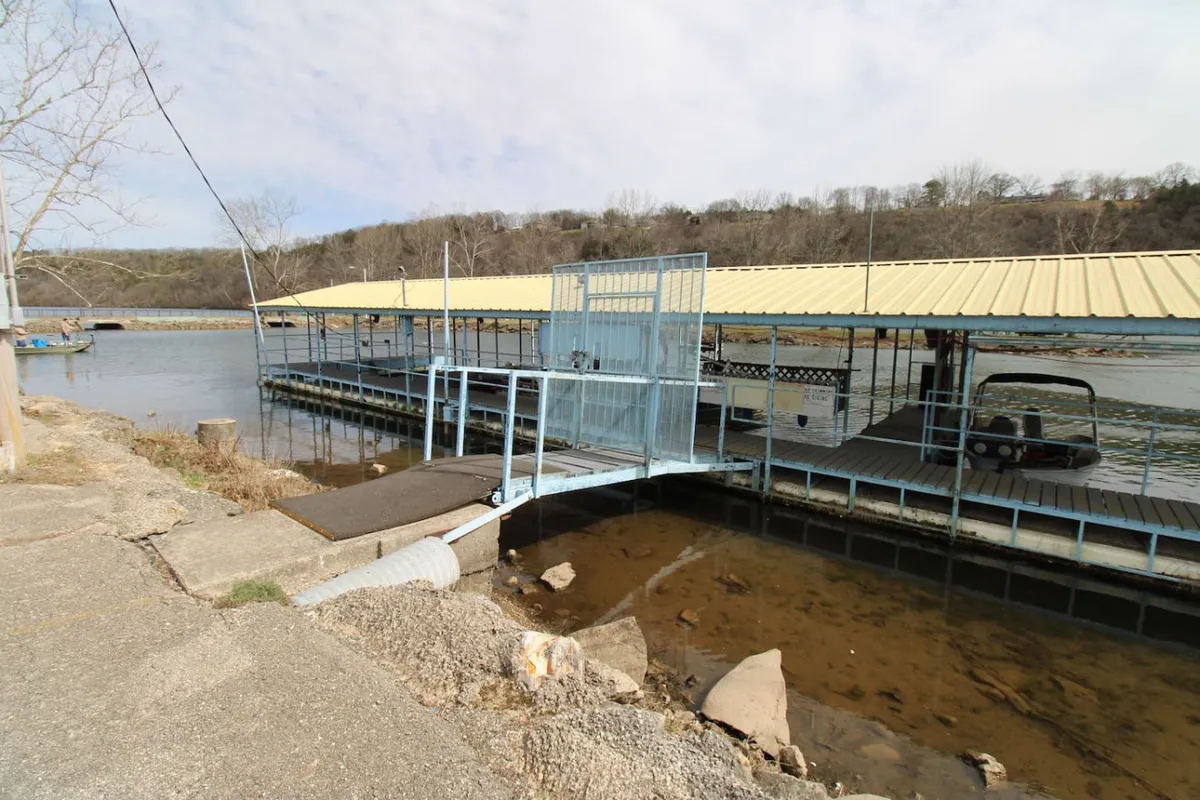 A serene dock with a yellow-roofed shelter extends out into the water, with a boat moored alongside. The view hints at early morning fishing outings, easy boat access, and the convenience of having a dedicated slip. The gentle light and peaceful setting capture the essence of lakeside leisure.