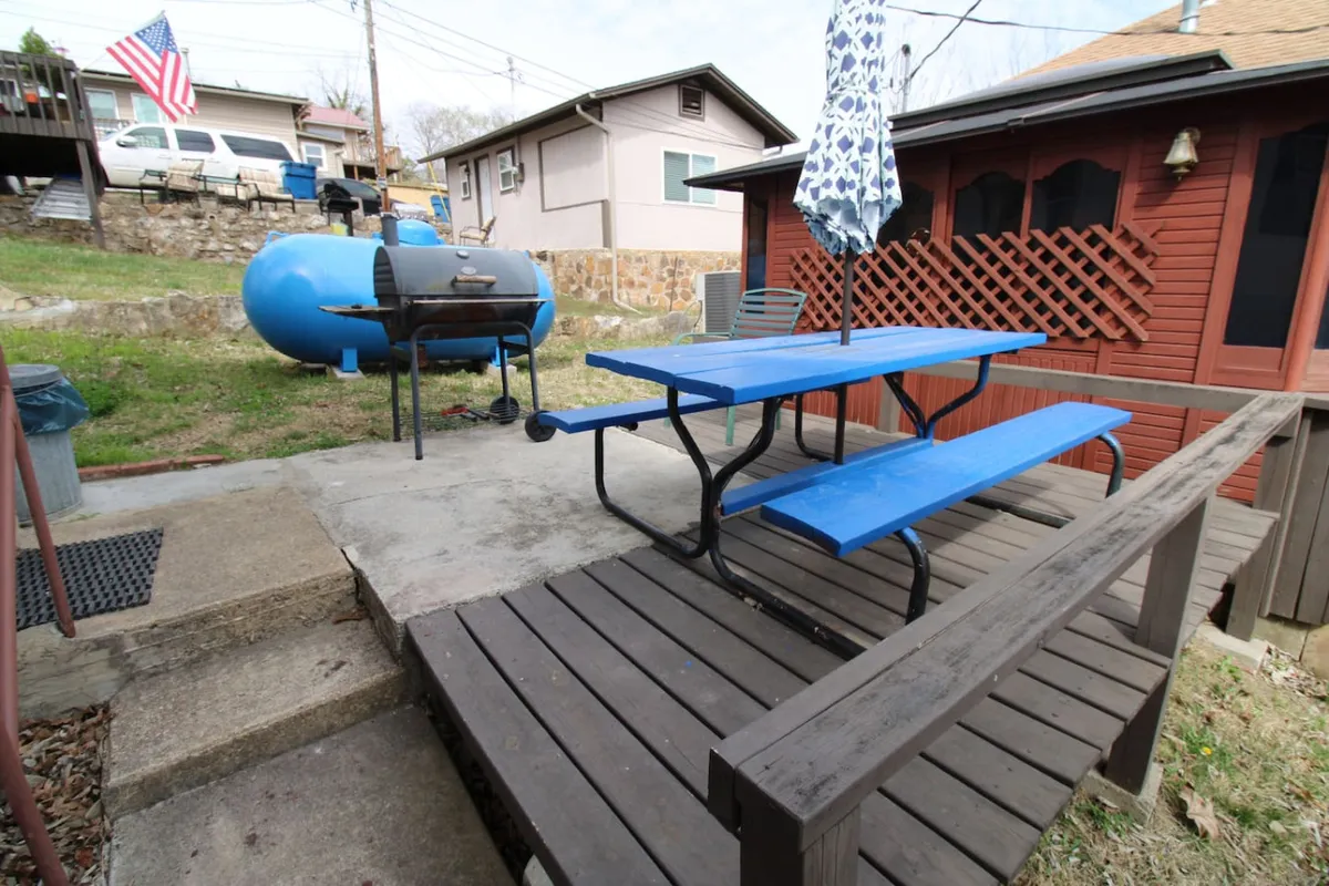An exterior view showing a blue picnic table and grill under an outdoor umbrella, with a flag and greenery in the background. The scene invites guests to take their culinary experience outdoors for barbecuing and picnicking, capturing the communal spirit and flexibility emphasized in the section.